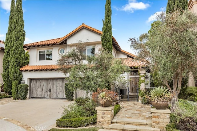 mediterranean / spanish-style home with a gate, driveway, stucco siding, a garage, and a tile roof