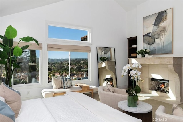 bedroom featuring a warm lit fireplace and high vaulted ceiling