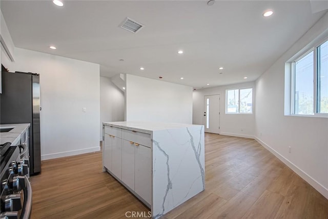 kitchen with appliances with stainless steel finishes, white cabinetry, light stone counters, light hardwood / wood-style floors, and a kitchen island