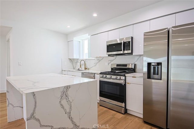 kitchen with appliances with stainless steel finishes, a center island, white cabinets, and light stone counters