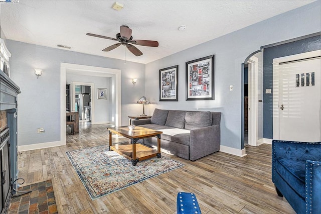 living room with a brick fireplace, a textured ceiling, hardwood / wood-style floors, and ceiling fan