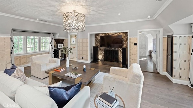 living room featuring wood-type flooring, ornamental molding, a chandelier, and vaulted ceiling