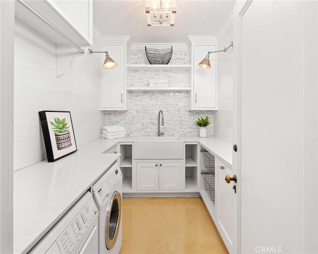 clothes washing area with crown molding, cabinets, sink, and washing machine and clothes dryer