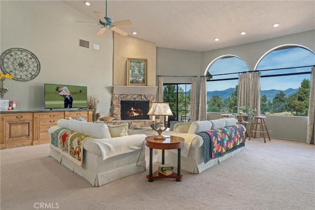 living room with a stone fireplace, light colored carpet, ceiling fan, and a high ceiling