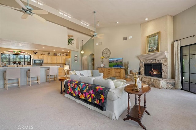 living room with light carpet, a fireplace, ceiling fan, and a high ceiling