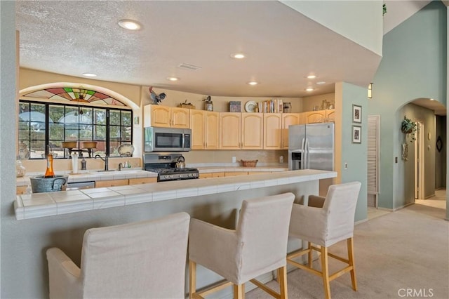 kitchen with tile countertops, a kitchen breakfast bar, kitchen peninsula, and appliances with stainless steel finishes