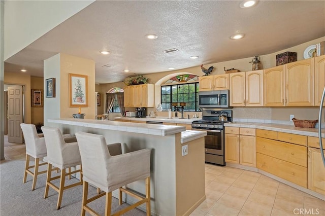 kitchen with stainless steel appliances, a breakfast bar area, tile counters, and light brown cabinets