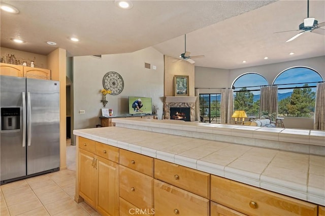 kitchen featuring ceiling fan, stainless steel refrigerator with ice dispenser, tile counters, light tile patterned flooring, and light brown cabinets