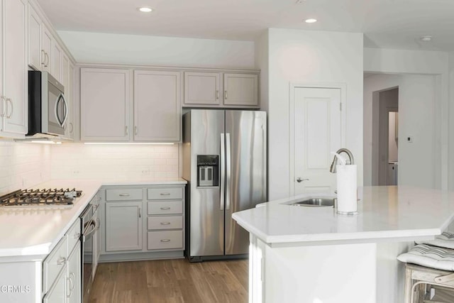 kitchen with sink, light hardwood / wood-style flooring, appliances with stainless steel finishes, an island with sink, and decorative backsplash