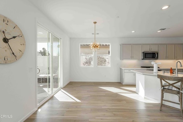 kitchen featuring decorative light fixtures, light hardwood / wood-style flooring, a kitchen breakfast bar, gray cabinets, and a notable chandelier