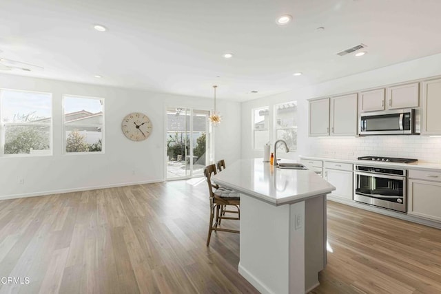 kitchen featuring appliances with stainless steel finishes, a kitchen island with sink, light hardwood / wood-style floors, and decorative light fixtures