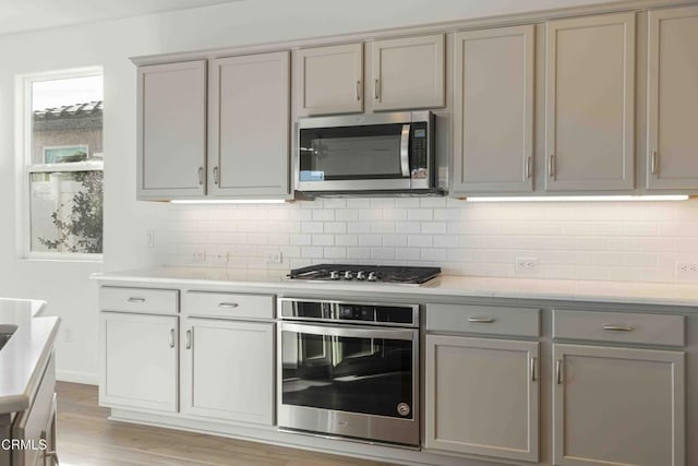 kitchen with stainless steel appliances, tasteful backsplash, gray cabinets, and light hardwood / wood-style floors