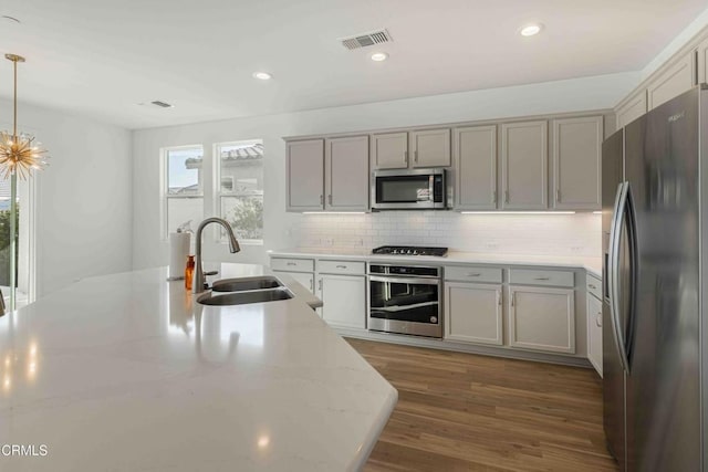 kitchen featuring sink, appliances with stainless steel finishes, gray cabinets, pendant lighting, and light stone countertops