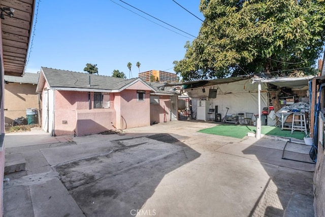 rear view of property with a patio area, a shingled roof, fence, and stucco siding