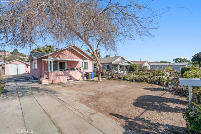 bungalow featuring a porch, stucco siding, a garage, an outdoor structure, and driveway