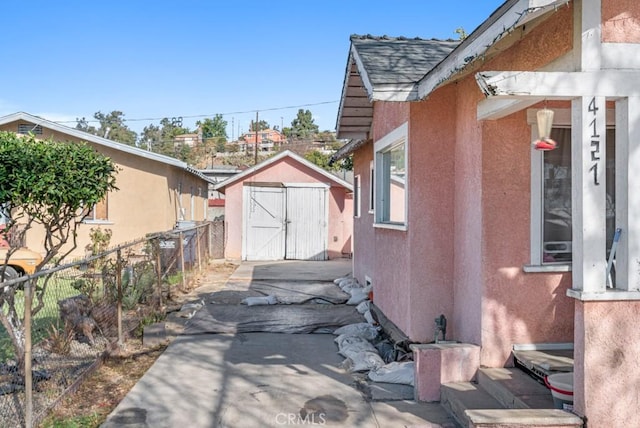 view of property exterior featuring a storage unit, fence, an outdoor structure, and stucco siding