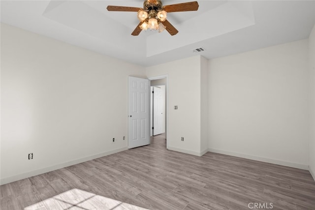 empty room with a tray ceiling, ceiling fan, and light wood-type flooring