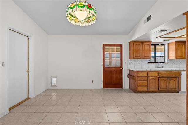 kitchen with light tile patterned flooring, pendant lighting, tile countertops, sink, and backsplash