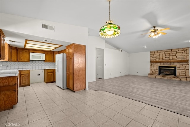 kitchen with light tile patterned floors, white appliances, hanging light fixtures, a stone fireplace, and vaulted ceiling