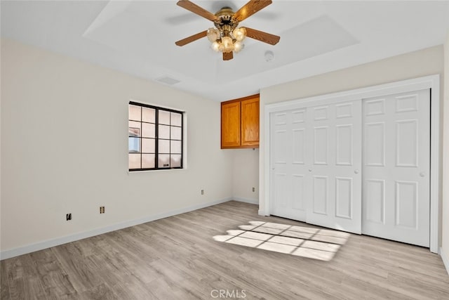 unfurnished bedroom with a closet, light hardwood / wood-style flooring, a raised ceiling, and ceiling fan