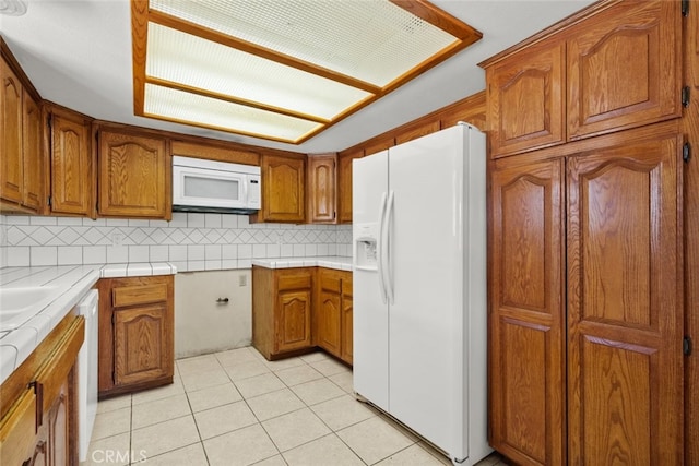 kitchen with light tile patterned flooring, tile countertops, backsplash, and white appliances