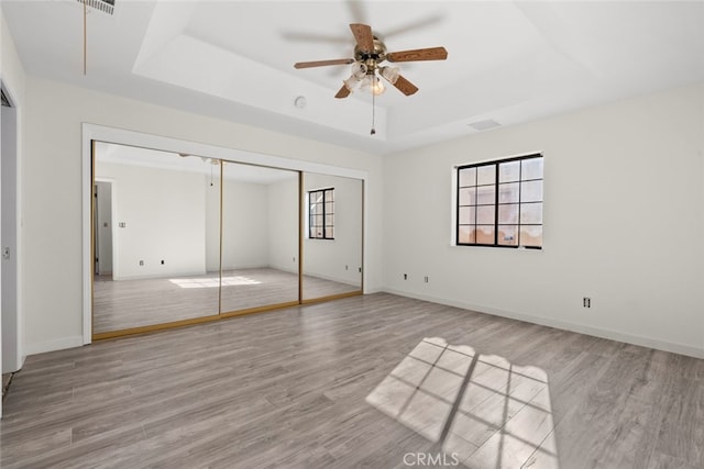 unfurnished bedroom with a closet, light hardwood / wood-style floors, ceiling fan, and a tray ceiling