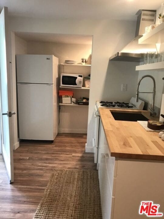 kitchen featuring dark wood-type flooring, butcher block counters, white appliances, wall chimney range hood, and white cabinets