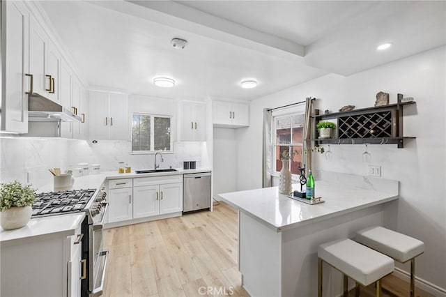 kitchen featuring under cabinet range hood, a peninsula, a sink, white cabinets, and appliances with stainless steel finishes