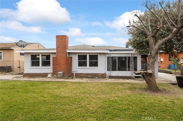 rear view of house with fence, a sunroom, a yard, stucco siding, and a chimney