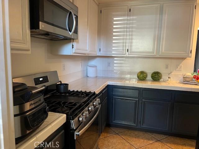 kitchen with tile counters, light tile patterned flooring, white cabinets, and appliances with stainless steel finishes