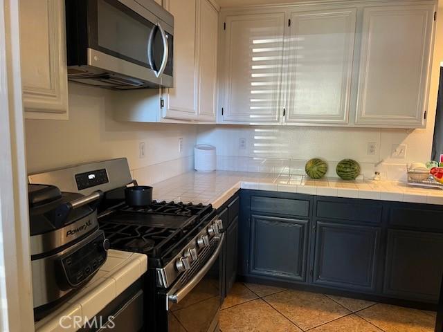 kitchen with appliances with stainless steel finishes, tile countertops, white cabinets, and light tile patterned floors