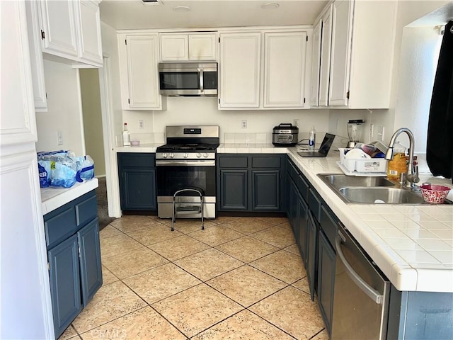 kitchen with appliances with stainless steel finishes, blue cabinets, sink, white cabinets, and light tile patterned floors