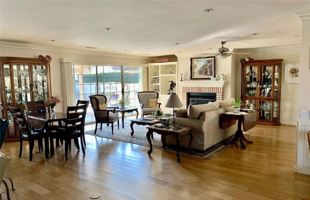 living room featuring light hardwood / wood-style flooring, a fireplace, ornamental molding, and ceiling fan