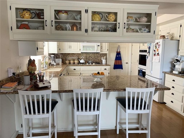 kitchen with white cabinetry, sink, white appliances, and a breakfast bar