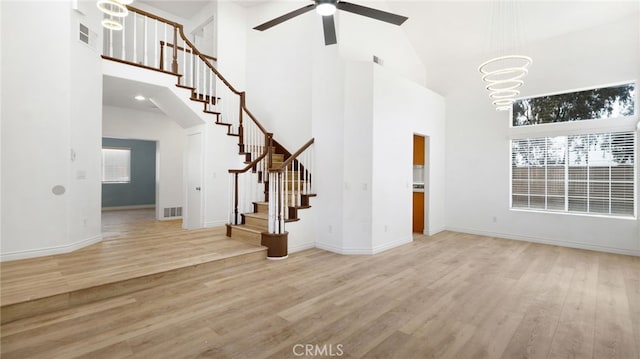 unfurnished living room featuring a towering ceiling, ceiling fan with notable chandelier, and light wood-type flooring