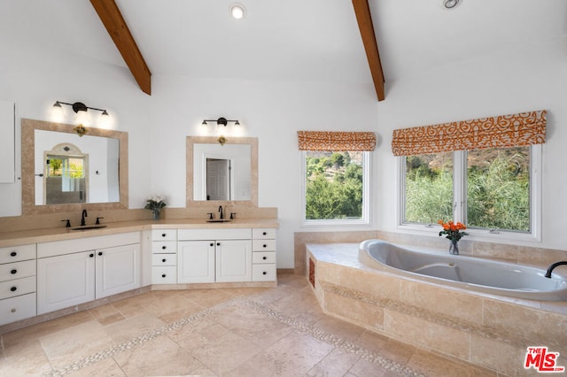 bathroom featuring beamed ceiling, vanity, tiled bath, and a wealth of natural light