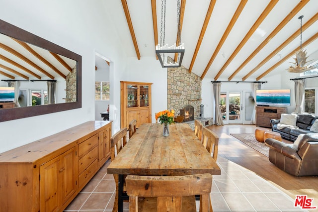 tiled dining space with beam ceiling, high vaulted ceiling, and a stone fireplace