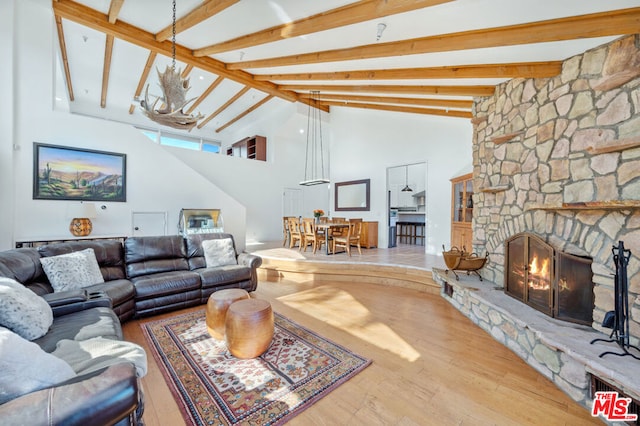 living room featuring hardwood / wood-style floors, beam ceiling, a stone fireplace, and high vaulted ceiling