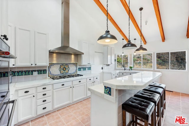 kitchen featuring decorative light fixtures, white cabinets, decorative backsplash, gas cooktop, and wall chimney range hood