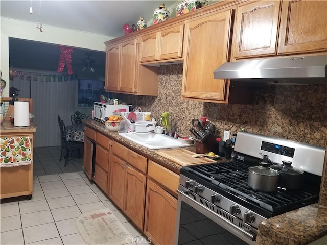 kitchen with light tile patterned floors, backsplash, white microwave, stainless steel gas stove, and under cabinet range hood