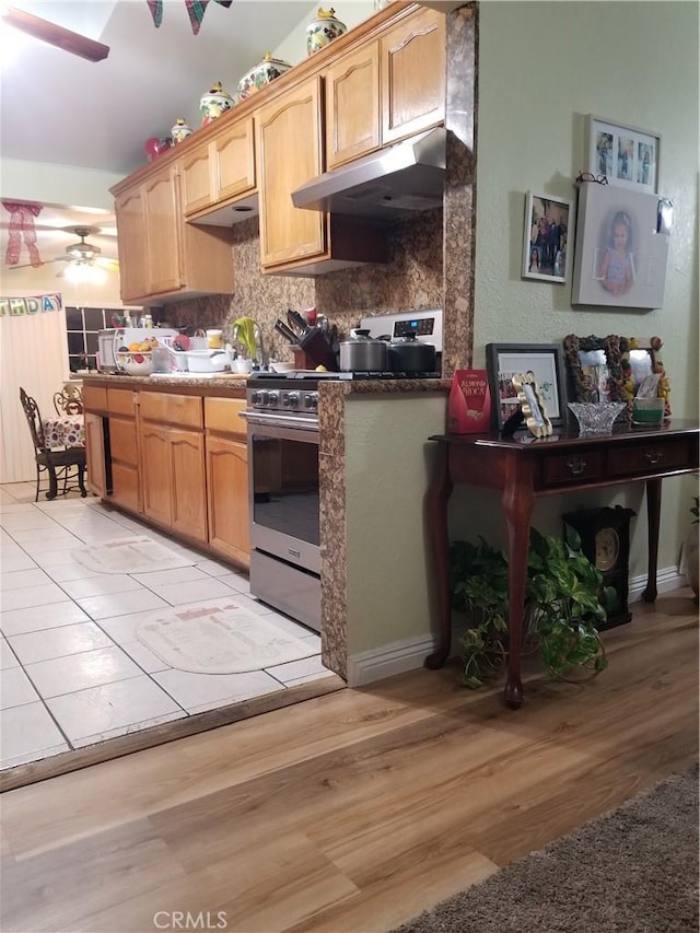 kitchen with decorative backsplash, ceiling fan, light wood-style flooring, under cabinet range hood, and stainless steel range with gas stovetop