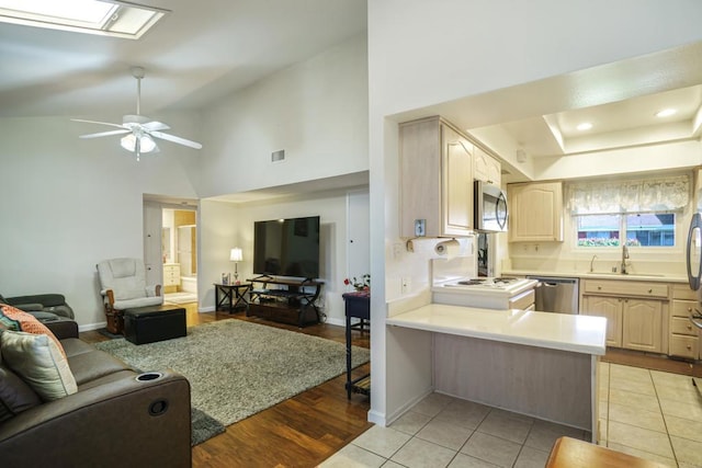 kitchen with a skylight, stainless steel appliances, light brown cabinetry, open floor plan, and a peninsula