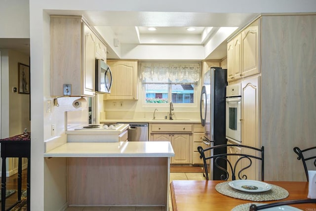 kitchen featuring stainless steel appliances, light countertops, a sink, and a peninsula