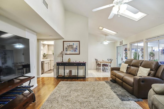 living area featuring lofted ceiling with skylight, wood finished floors, visible vents, and a ceiling fan