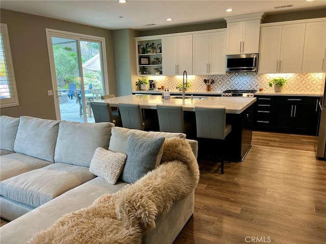 kitchen featuring sink, white cabinetry, a center island with sink, light hardwood / wood-style floors, and backsplash