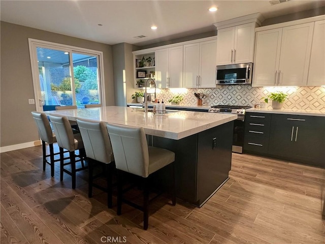 kitchen with stainless steel appliances, an island with sink, and white cabinets