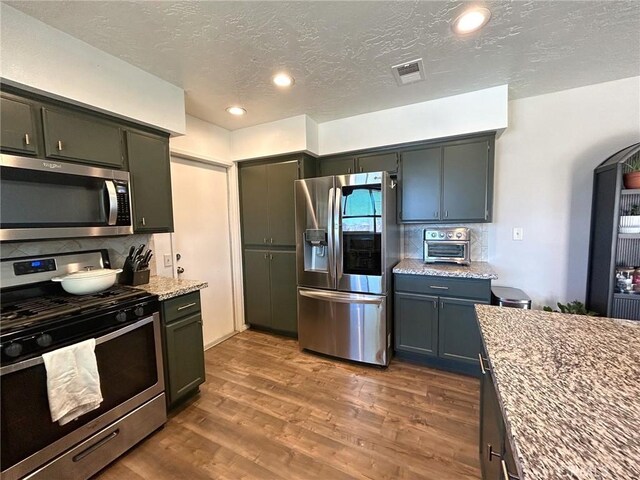 kitchen featuring light stone counters, stainless steel appliances, wood finished floors, visible vents, and decorative backsplash