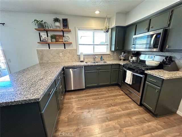 kitchen with light stone counters, backsplash, light wood-style flooring, appliances with stainless steel finishes, and a sink