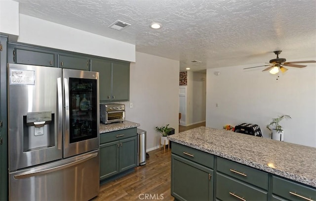 kitchen with light stone countertops, dark hardwood / wood-style floors, stainless steel fridge, and green cabinetry