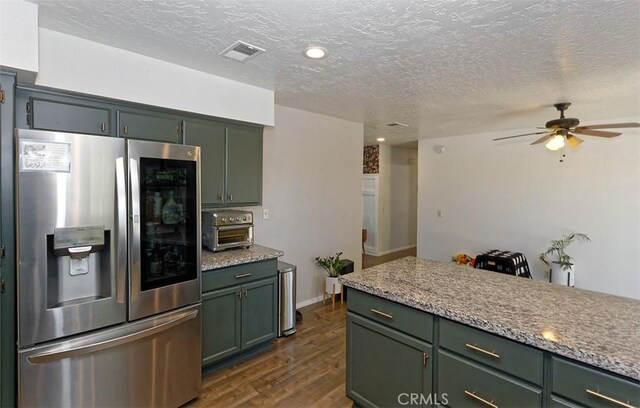 kitchen featuring a toaster, visible vents, green cabinets, dark wood-style floors, and stainless steel fridge